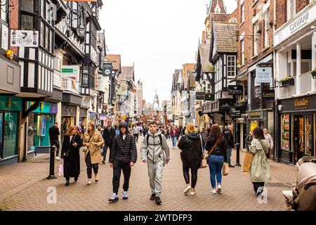 Shopper, die über nasse Gehwege und Kopfsteinpflaster in der römischen Stadt Chester England spazieren, um das mittelalterliche Kreuz und die Geschäfte in den Reihen Stockfoto