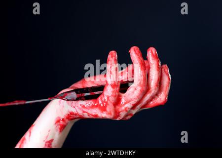 Blutige Hand, die ein Messer mit Blut auf schwarzem Hintergrund hält. Mordkonzept häuslicher Gewaltmissbrauch Stockfoto