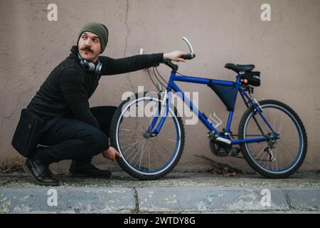 Stilvoller Stadtmann mit einem Fahrrad an einer Wand Stockfoto