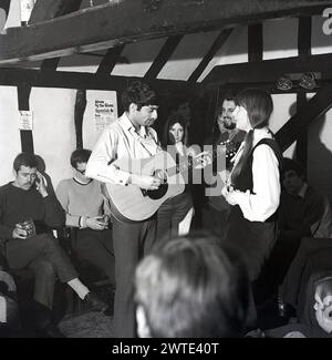 1970, historische Volksmusik, eine Musikerin, die Gitarre spielt, und eine Sängerin, die in einem alten Pub in England, Großbritannien auftritt. Stockfoto