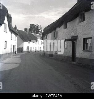1950er Jahre, historische, englische Dorf High Street in Devon, zeigen traditionelle Strohdach-Terrassenhäuser aus Stein, England, Großbritannien. Auf einem Schild oben an der Wand steht dann "Public Telephone". Stockfoto