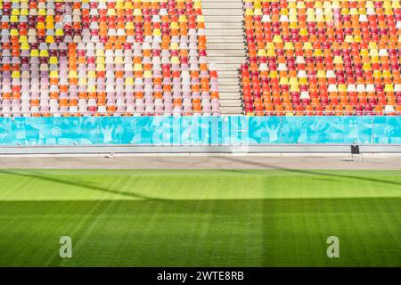 Leeres Stadion mit farbigen Stühlen in Tribüne und dem grünen Rasenrasen Stockfoto