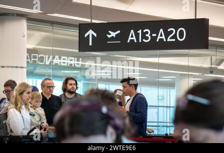 TORONTO, KANADA - 03 10 2024: Ein schwarzes Schild mit weißen Buchstaben der Gate-Nummer mit einer Gruppe von Reisenden darunter, die in einem überfüllten Land auf das Einsteigen warten Stockfoto