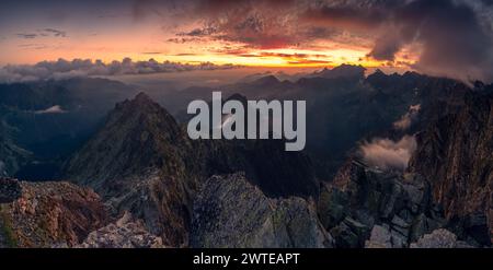 Dramatischer Sonnenaufgang auf dem Rysy-Gipfel im Tatra-Gebirge. Roter Himmel mit dynamischen Wolken und Nebel über felsigen Gipfeln. Moos bedeckte Steine im Vordergrund. Stockfoto