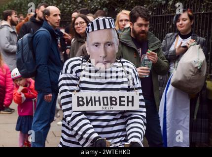 London, Großbritannien. März 2024. Ein als Putin gekleideter Demonstrant in Gefängniskleidung und Handschellen läuft vor der russischen Botschaft vorbei an russischen Bürgern, die sich um ihre Stimme schlangen, während Wahlen in Russland stattfinden. Quelle: Vuk Valcic/Alamy Live News Stockfoto