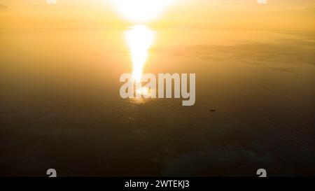 Eine Person, die am Strand zu einer untergehenden Sonne am Horizont läuft Stockfoto