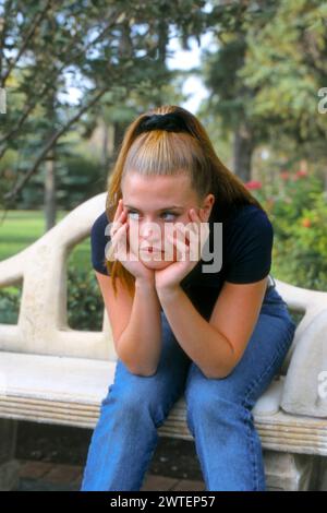 Eine junge blonde, launische Teenagerin, die auf einer Parkbank sitzt Stockfoto