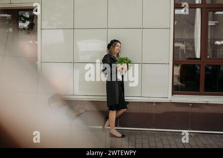 Eine Frau steht vor einer Wand und hält einen Haufen frisches Gemüse in der Hand. Stockfoto