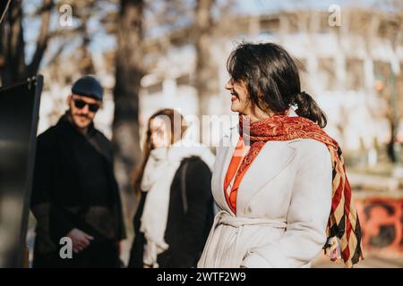 Außenporträt einer freudigen Frau mit einem lebendigen Schal, die einen sonnigen Tag in der Stadt genießt, während die Menschen in einem verschwommenen Hintergrund vorbeigehen. Stockfoto