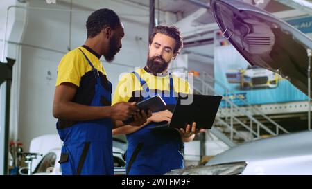 Mechaniker im Kfz-Service bestellen neue Teile für beschädigte Fahrzeuge mit Laptop und Tablet. Kollegen, die online nach Komponenten suchen, die alte ersetzen können, wenn ein Auto nicht funktioniert Stockfoto