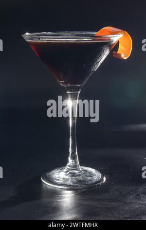 Ein Martini-Glas mit einer Scheibe Orangenschale darauf. Das Glas ist mit einer dunklen Flüssigkeit gefüllt Stockfoto