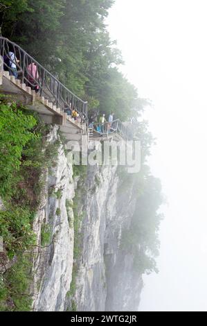 Touristen spazieren entlang des Cliff Hanging Walkway, der sich an den Kanten der senkrechten Klippe der Gipfel des Tianmen Berges anschmiegt. Stockfoto