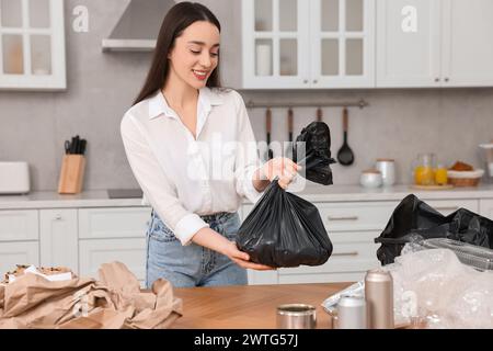Müllsortierung. Lächelnde Frau mit Plastiktüte am Tisch in der Küche Stockfoto