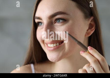 Lächelnde Frau, die Sommersprossen mit Stift im Haus zeichnet, Nahaufnahme Stockfoto