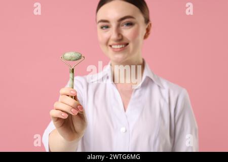 Kosmetologe mit Gesichtsrolle auf rosa Hintergrund, selektiver Fokus Stockfoto