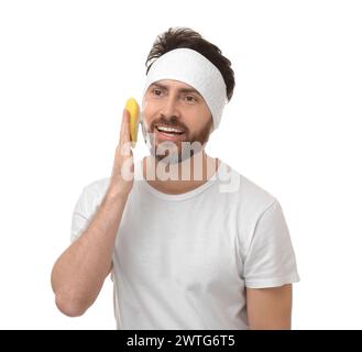 Mann mit Stirnband, der sein Gesicht mit Schwamm auf weißem Hintergrund wäscht Stockfoto