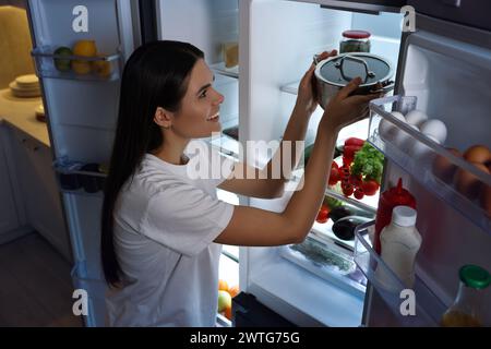 Eine junge Frau, die nachts in der Küche Topf aus dem Kühlschrank nimmt, über dem Blick Stockfoto