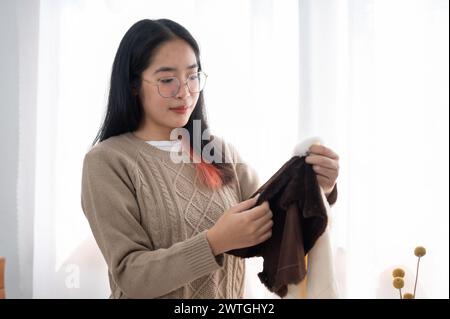 Eine positive asiatische Frau, die Stoff auf ihre Handwerkskleidung überprüft und Nähzubehör am Tisch vorbereitet. Handarbeit, Stickerei, Schneider Stockfoto