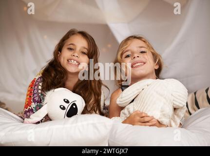 Fröhliche Übernachtung und Porträt von Kindern im Schlafzimmer zum Spielen, Binden und Entspannen mit Spielzeug zu Hause. Nacht, Freunde und junge Mädchen im Bett im Zelt Stockfoto