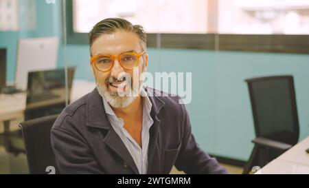 Reifer Mann, der in einem Coworking Desk arbeitet und lächelt Stockfoto