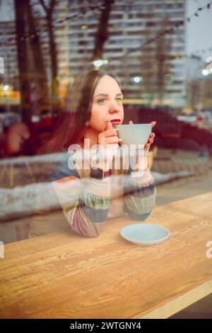 Eine Frau sitzt friedlich an einem Tisch, schlürft elegant an einer Tasse, während sie einen Moment der Entspannung in einem belebten Café genießt Stockfoto