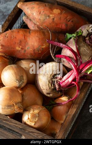Gemüse, Süßkartoffelzwiebeln und Rote Bete in einer Kiste aus Holz und Draht. Auf dunklem Steingrund Stockfoto