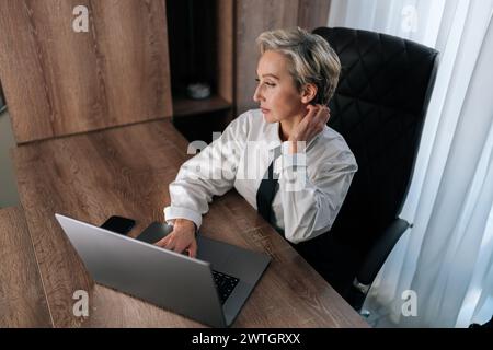 Blick von oben auf eine ermüdete, elegante Geschäftsfrau mit Nackenschmerzen, eingeklemmten Nerven, verspannten Muskeln und zervikaler Osteochondrose. Müde Unternehmerin Stockfoto