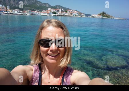 Eine Reisende mit Sonnenbrille macht Selfie mit türkisfarbenem Wasser der Ägäis auf der Insel Samos, Griechenland Stockfoto