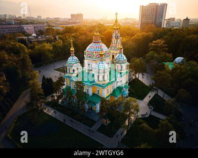 Luftdrohnen-Panorama der Ascension Cathedral Russisch-orthodoxe Kirche und Schneeberge im Hintergrund im Panfilov Park vor Sonnenuntergang Himmel in Almat Stockfoto