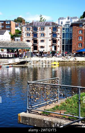 Blick über den Fluss exe zu Geschäften und Restaurants entlang des East Quay mit Lovelocks auf einem Zaun im Vordergrund, Exeter, Devon, Großbritannien, Europa. Stockfoto