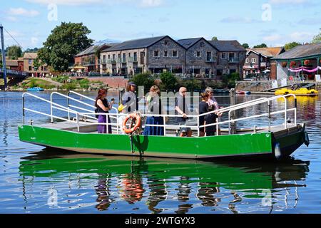 Passagiere an Bord von Butts Ferry überqueren den Fluss exe mit dem East Bank Quay und Restaurants und Geschäften auf der Rückseite, Exeter, Devon, Großbritannien, Europa. Stockfoto