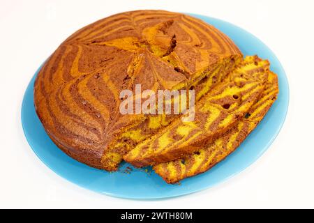 Ein Stück Zebrakuchen wird in zwei Hälften geschnitten und liegt auf einer blauen Platte. Der Kuchen ist mit einem Zebramuster dekoriert und hat ein gelbes und braunes Farbschema Stockfoto