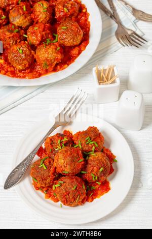 Albondigas, spanische Fleischbällchen aus Schweinefleisch und Rindfleisch in Tomatensoße mit roter Paprika und Zwiebelsauce, bestreut mit Schnittlauch auf weißem Holz Stockfoto