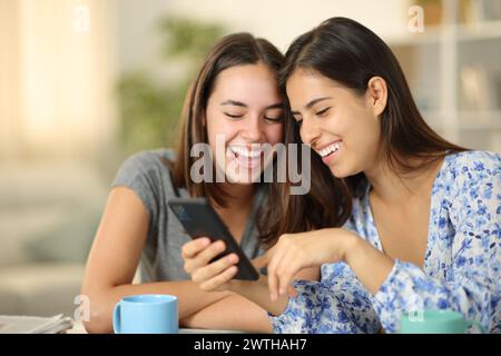 Glückliche Frauen, die Online-Inhalte am Telefon überprüfen und zu Hause lachen Stockfoto