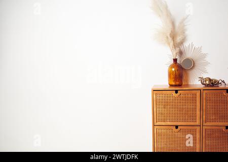 Schönes Modell, weiße Wand für Ihr Poster, Strauß getrockneter Pampas-Grasblumen in einer Vase, Spiegel, Bronzekäfer auf Schubladen. Hintergrund mit Kopierraum, leer. Vorlage für Ihr Design Stockfoto