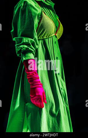 Interessantes, farbenfrohes Outfit, grünes Kleid, pinkfarbene Handschuhe auf schwarzem Hintergrund Stockfoto