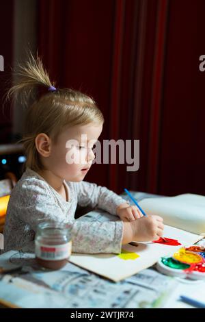 Ein junges Künstlerbild mit Aquarellen. Das entzückende blonde Mädchen von 2,5 Jahren lernt zu Hause am Tisch zu malen. Stockfoto