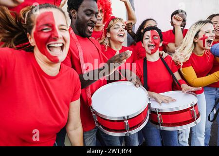 Multirassische Sportfans singen, während sie ihre Mannschaft unterstützen - Fußballfans, die Spaß außerhalb des Stadions mit roten T-Shirts haben - Event und Wetten Stockfoto