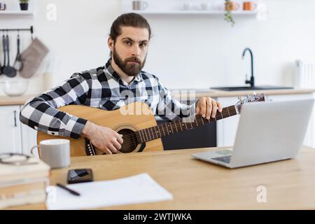 Bärtiger Erwachsener posiert mit Gitarre und genießt einen angenehmen Zeitvertreib zu Hause. Stockfoto