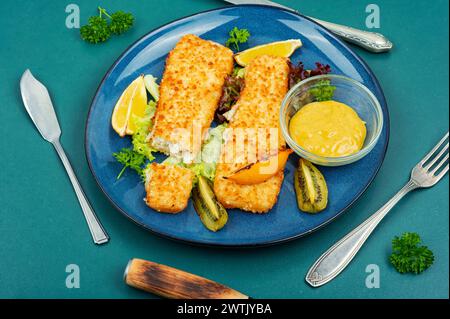 In Semmelbröseln gebratenes Pollock-Filet mit Soße und Kiwi. Fisch in Chips. Stockfoto