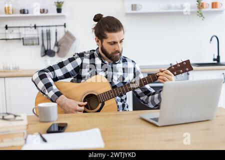 Bärtiger Erwachsener posiert mit Gitarre und genießt einen angenehmen Zeitvertreib zu Hause. Stockfoto