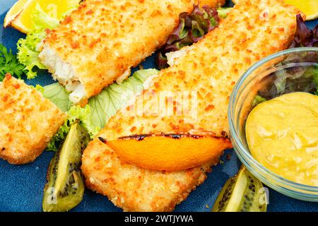 Pollock-Filet in Semmelbröseln geröstet, serviert mit Sauce und Kiwi. Nahaufnahme. Stockfoto