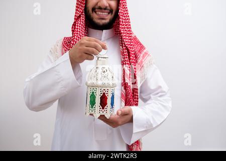 Ein arabischer Mann trägt die würdevolle Kleidung von Kandoura und Keffiyeh und erweitert ein Symbol der Gastfreundschaft und Großzügigkeit, indem er Fanous hält. Gegen eine bac Stockfoto