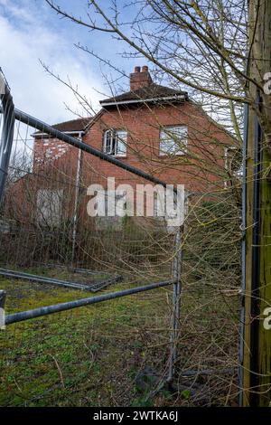 Ein leeres und verschlossenes Haus wartet auf den Abriss, mit einem hohen Drahtzaun, der jeden abhält, der sich dem Ort nähert. Stockfoto