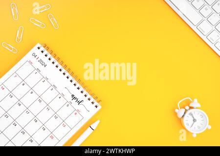 April 2024, monatlicher Schreibtischkalender für 2024 Jahre und Wecker mit Büroklammern auf gelbem Hintergrund. Position mit Kopierraum. Stockfoto