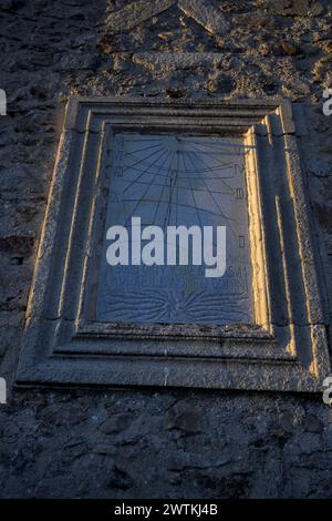 Steinsonnenuhr und römische Ziffern an der alten Steinmauerfassade vertikal Stockfoto