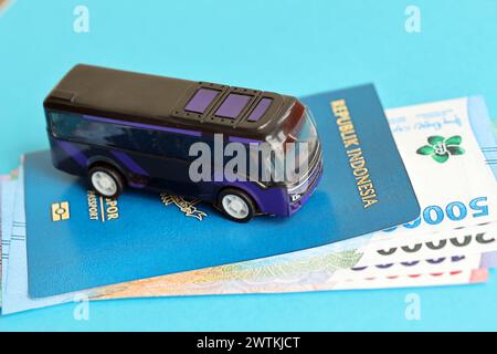 Blauer Indonesien-Pass mit Geld und Spielzeugbus auf blauem Hintergrund Nahaufnahme. Tourismus und Reisekonzept Stockfoto