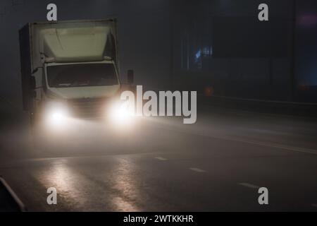 Ein Lkw mit Scheinwerfern fährt um Mitternacht auf einer nebeligen Autobahn Stockfoto
