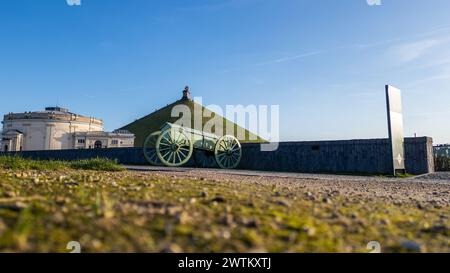 Waterloo, Brüssel, Belgien, 25. Februar 2024 dieses Bild bietet eine einzigartige Bodenperspektive einer historischen Kanone auf dem Waterloo-Schlachtfeld mit dem Löwenhügel im Hintergrund. Die Kanone ist links positioniert, was auf ihre einst wichtige Rolle in der Schlacht hindeutet. Der Löwenhügel erhebt sich in der Ferne, in der Mitte des Rahmens, auf dem die Löwenstatue sichtbar ist. Der Vordergrund zeigt das strukturierte Gras und verleiht der Umgebung ein natürliches Gefühl. Der klare blaue Himmel darüber gibt dem Bild einen ruhigen Ton, der reich an historischer Symbolik ist. Blick vom Boden auf Waterloo Canno Stockfoto