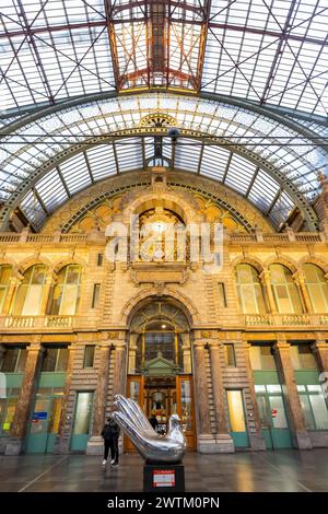 Antwerpen, Belgien, 25. Januar 2024, dieses Bild zeigt die herrliche Verschmelzung von Kunst und architektonischem Erbe im Atrium des Antwerpener Hauptbahnhofs. Im Vordergrund steht eine moderne silberne Skulptur, die die Aufmerksamkeit vor dem Hintergrund des klassischen Steinmetzes und der kunstvollen Uhr unter der aufwändigen Eisen- und Glasdecke auf sich zieht. Die Anwesenheit von Zuschauern verleiht der historischen Umgebung ein größeres Maß und menschliches Interesse. Kunst und Architektur im Antwerpener Hauptbahnhof Atrium. Hochwertige Fotos Stockfoto